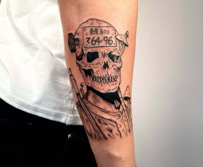 Tattoo of a grim skull with mechanical elements, showcasing psychedelic art on the forearm.