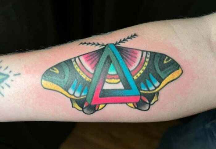 Psychedelic art tattoo of a colorful butterfly with a geometric triangle design on an arm.
