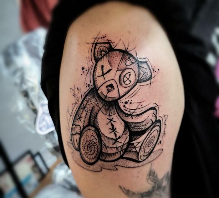Psychedelic art tattoo of a surreal teddy bear design on an arm, featuring intricate line work and abstract elements.