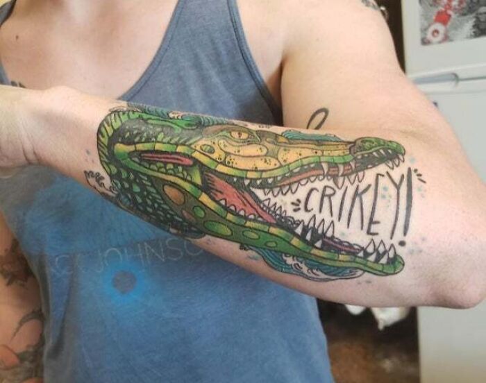 Colorful psychedelic tattoo of a crocodile on an arm, displaying vibrant trippy art style.