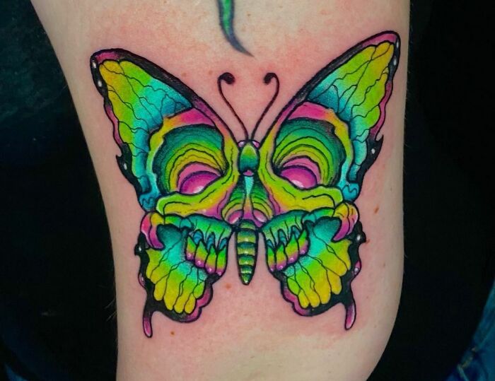 Colorful trippy tattoo of a psychedelic butterfly, featuring vibrant hues of green, blue, and pink.