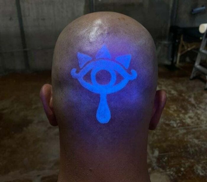Glowing psychedelic tattoo on the back of a bald head in a dimly lit room.