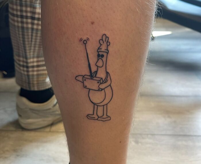 Funny chicken leg tattoo resembling a cartoon character holding a remote control.