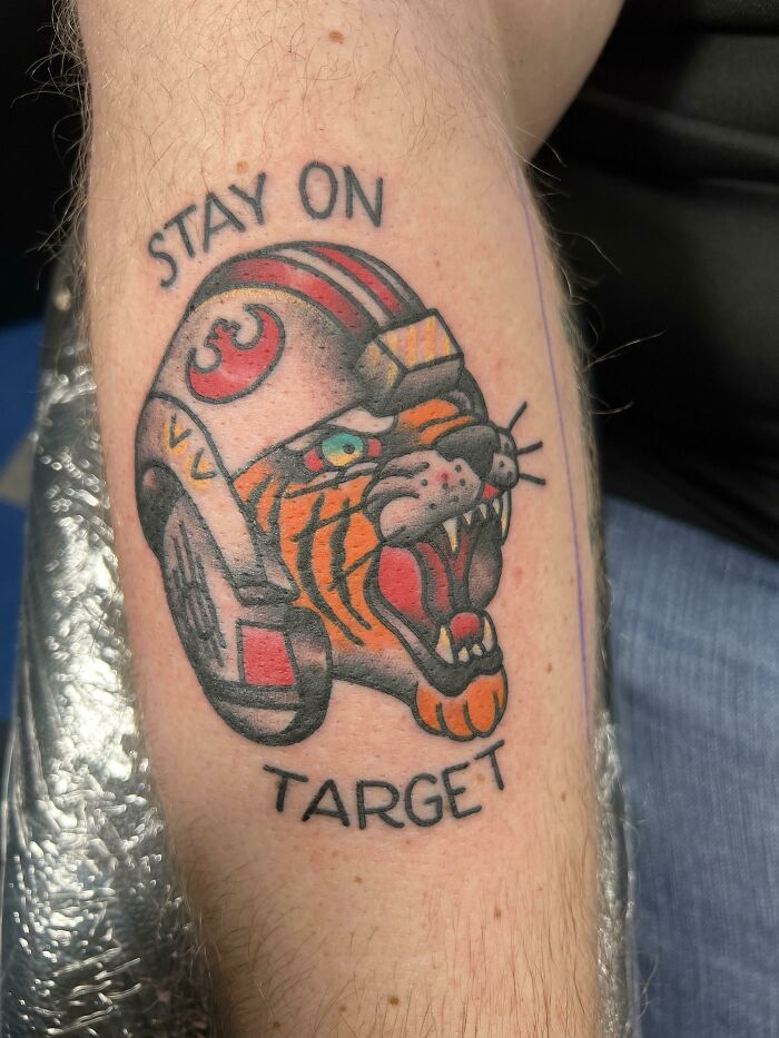 Colorful tattoo featuring a roaring tiger in a helmet with the words "Stay on Target"; creative word tattoo inspiration.