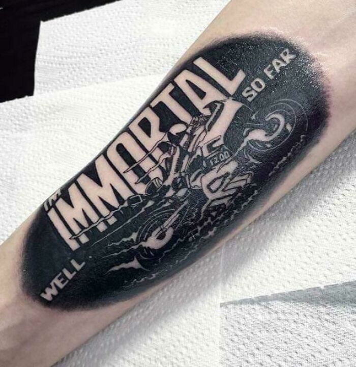 Tattoo of a motorcycle with "Immortal So Far" text, showcasing creative word tattoos for inkspiration.