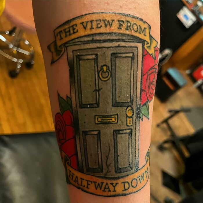 Tattoo of a door with roses and a banner reading "The View From Halfway Down," symbolizing deep personal meaning.
