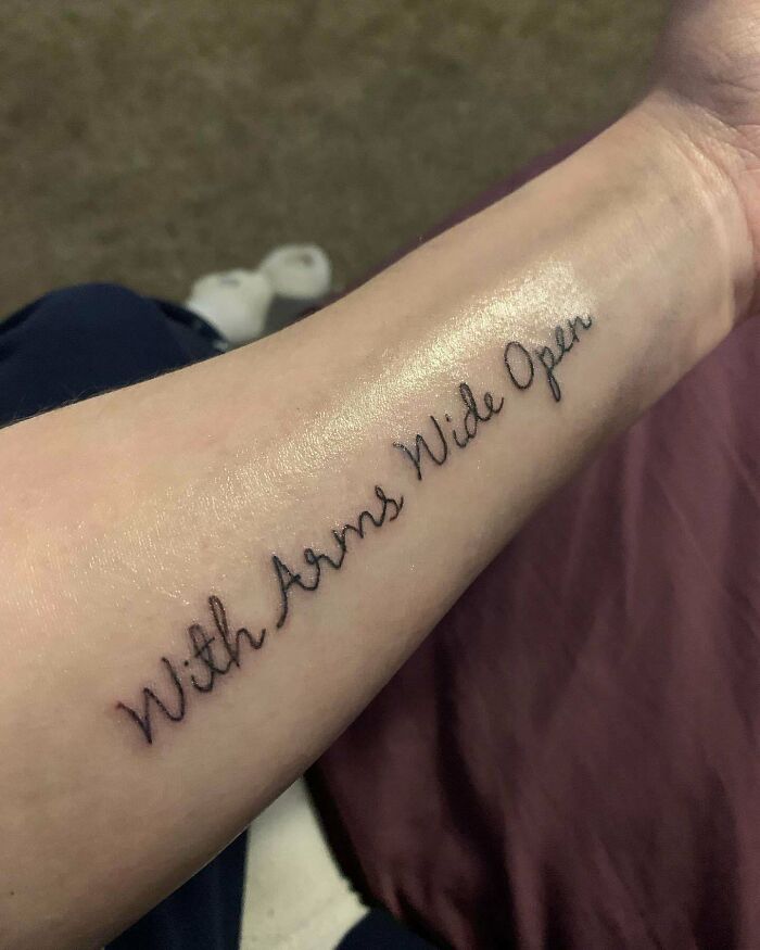 Word tattoo on forearm reading "With Arms Wide Open," showcasing creative inkspiration.