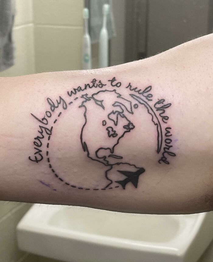 Word tattoo saying "Everybody wants to rule the world" with a globe and plane design on arm.