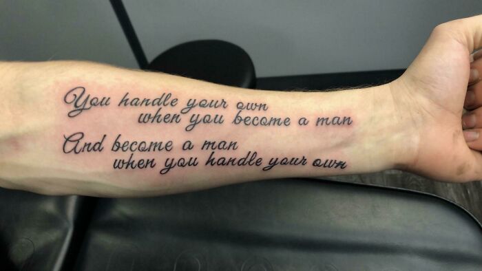 Arm with a word tattoo in elegant script, featuring an inspirational quote about maturity and self-reliance.