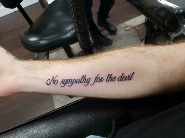 Tattoo on forearm reads "No sympathy for the devil," showcasing a word tattoo idea for new ink.