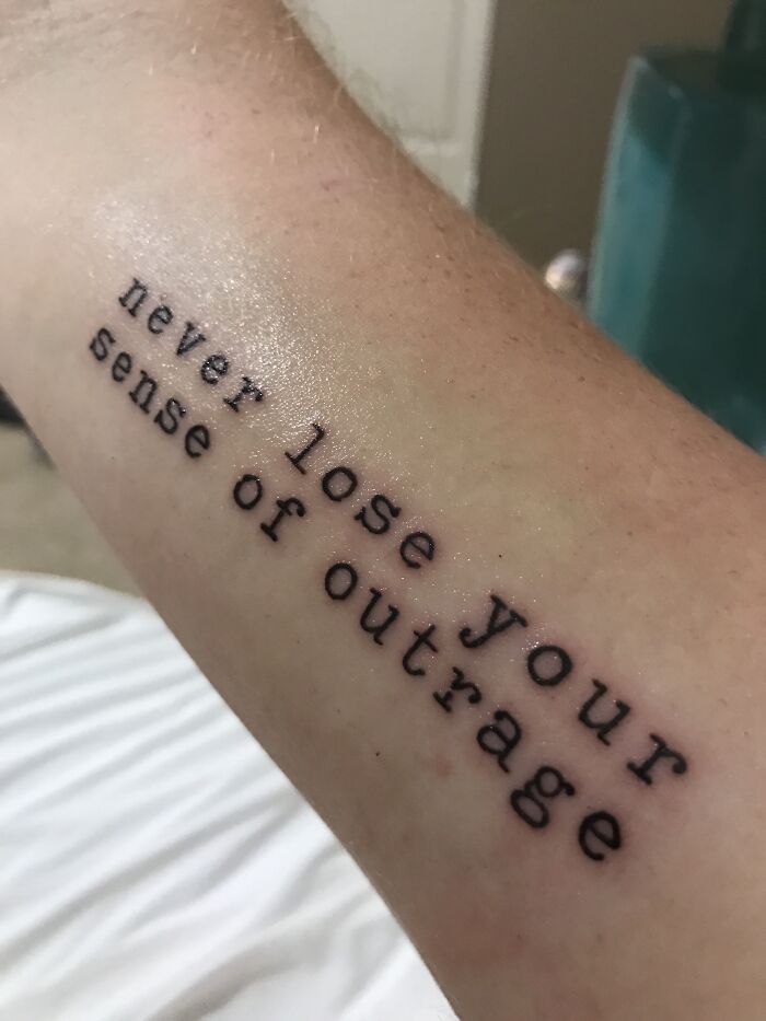 Tattoo with the words "never lose your sense of outrage" on forearm, representing creative word tattoos.