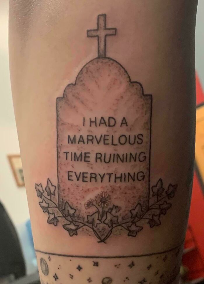 Tattoo of a gravestone with text "I had a marvelous time ruining everything," surrounded by ivy design.