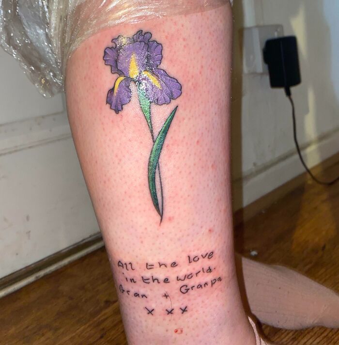 Floral word tattoo featuring a purple flower and sentimental text on a person's leg.