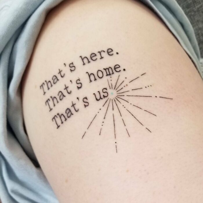 Minimalist word tattoo reading "That's here. That's home. That's us." with starburst design.