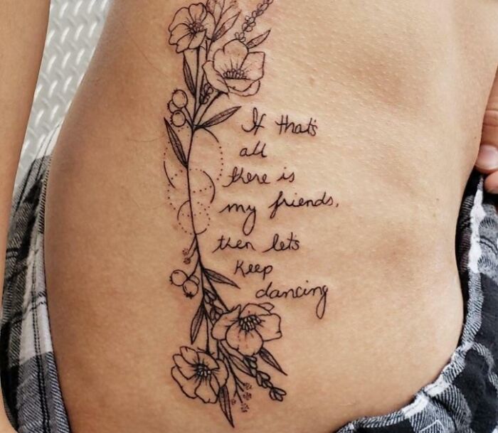 Floral and text tattoo on a person's side with inspirational words about friendship and dancing.