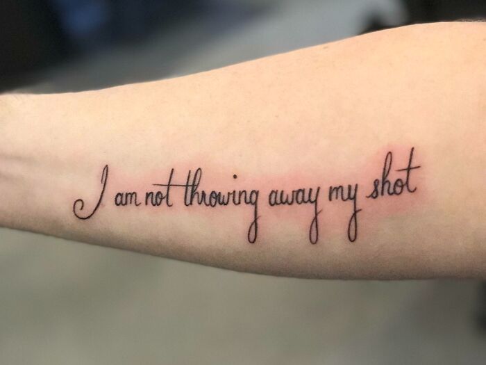 Word tattoo saying "I am not throwing away my shot" on an arm, showcasing creative inkspiration.