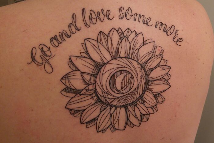 Word tattoo idea featuring a sunflower and the phrase "Go and love some more" intricately inked on skin.