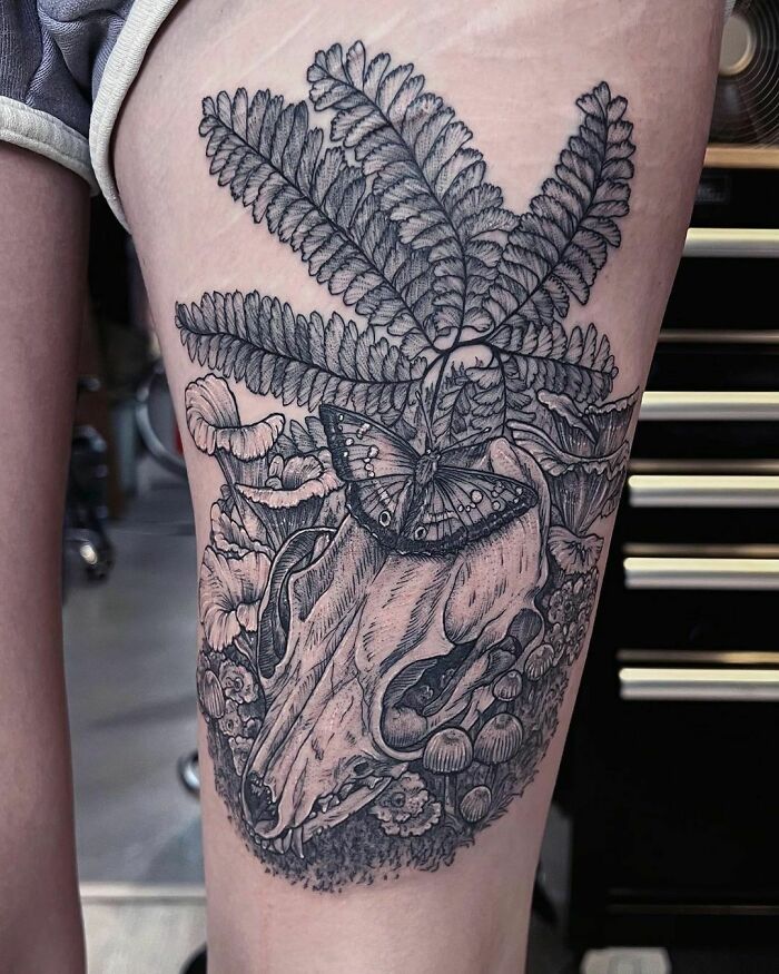 Detailed nature tattoo with skull, ferns, and butterfly on upper thigh, capturing a wild side.