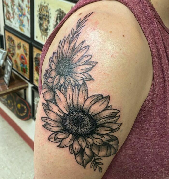 Sunflower nature tattoo on upper arm, black ink design in a tattoo parlor setting.
