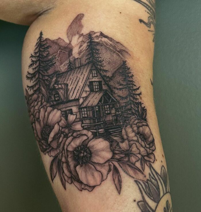 Nature tattoo of a cabin, trees, and flowers on an arm, depicting a wild and serene landscape.