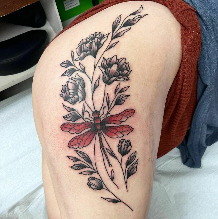 Nature tattoo featuring a red dragonfly and black flowers on an upper arm, celebrating the wonders of Mother Earth.
