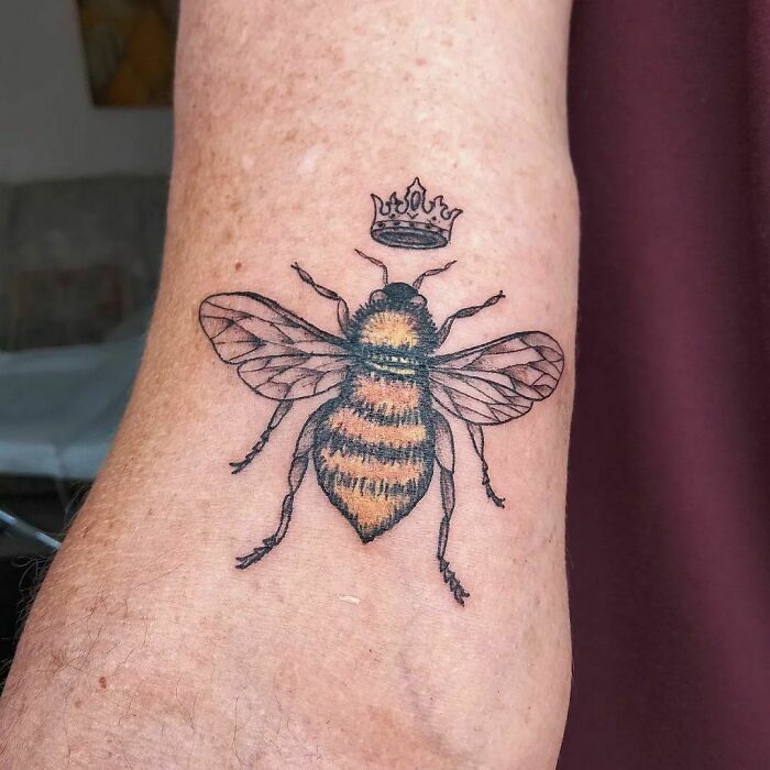 A bee tattoo with a crown on a person's arm, showcasing nature tattoos with a wild side.