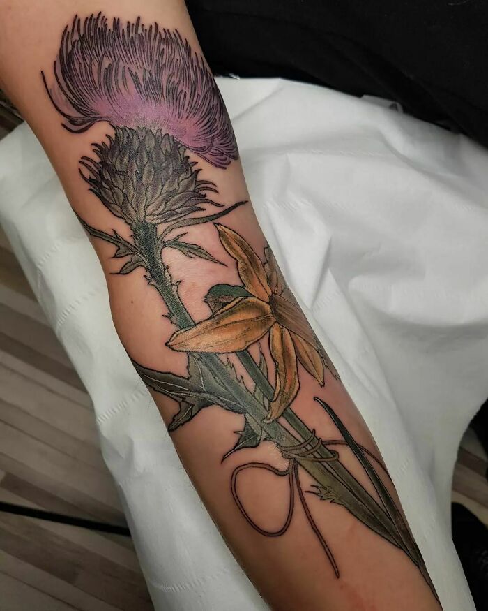 Nature tattoo with a detailed thistle and lily design on an arm.
