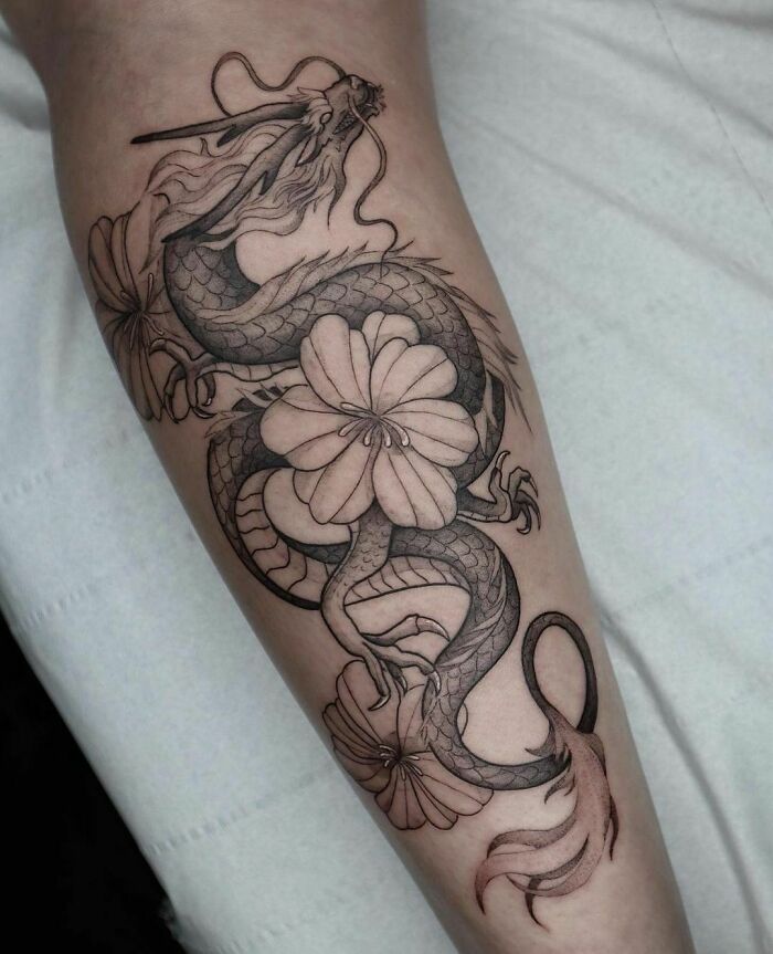 Intricate nature tattoo featuring a dragon entwined with flowers on a person's forearm.