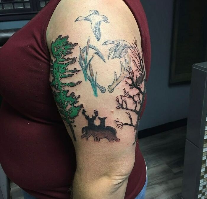 Nature tattoo depicting deer, birds, trees, and antlers on upper arm, showcasing a wild side theme.