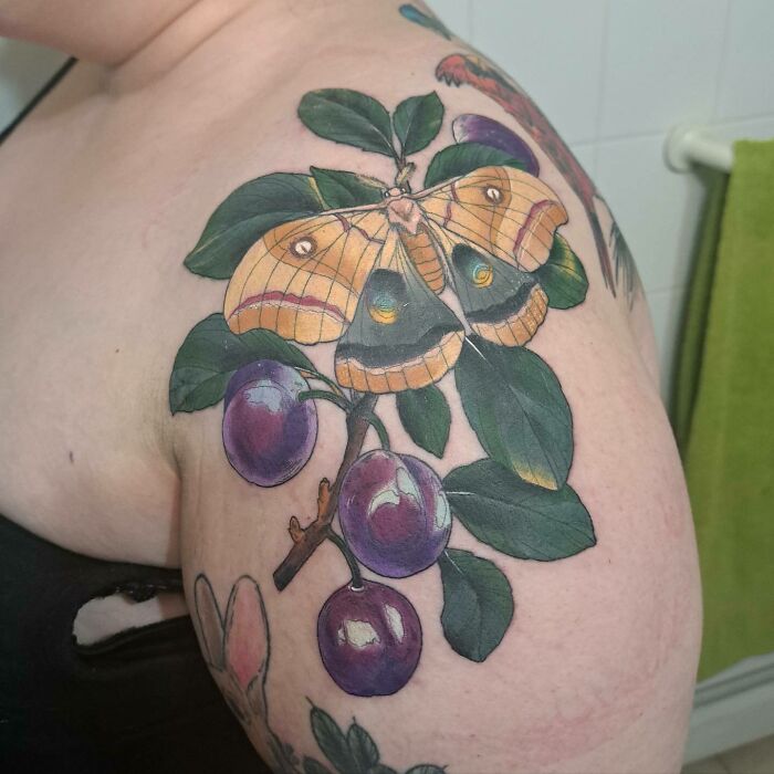 Nature tattoo of a butterfly and plums on a person's shoulder.