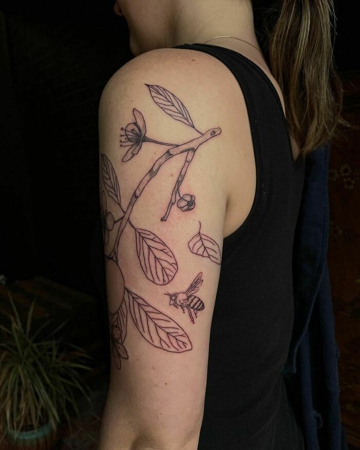 Nature tattoo featuring a botanical design with a branch and bee on a person's upper arm.