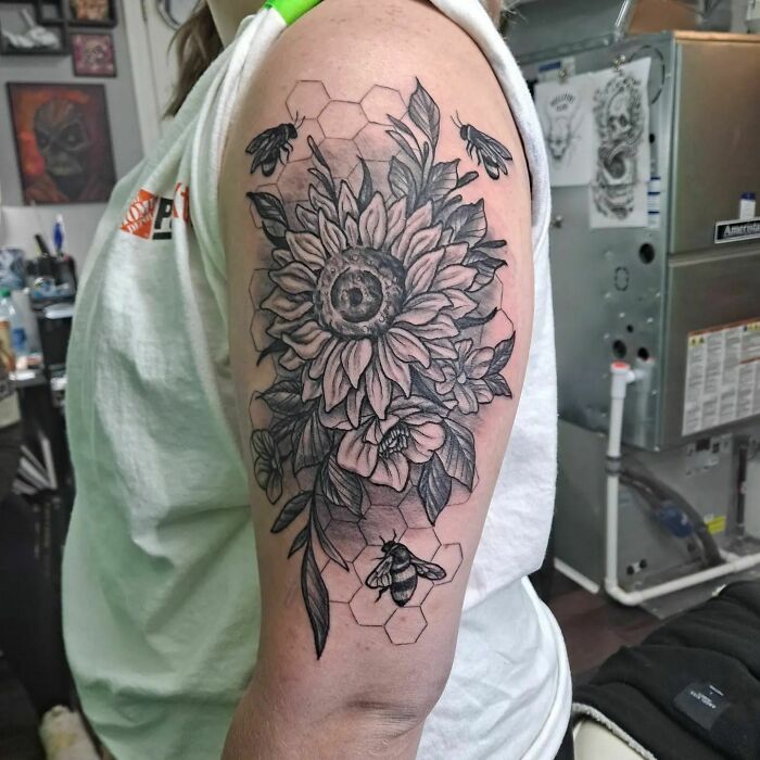 Nature tattoo featuring a sunflower, bees, and hexagons on a person's arm.