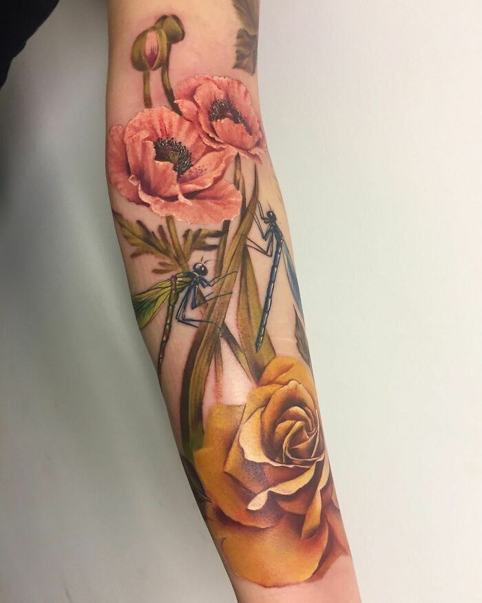 Nature tattoo featuring poppies, dragonflies, and a rose on an arm.