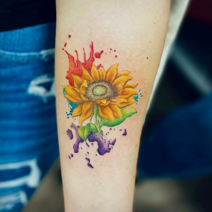 Colorful sunflower nature tattoo on forearm with splashes of paint.