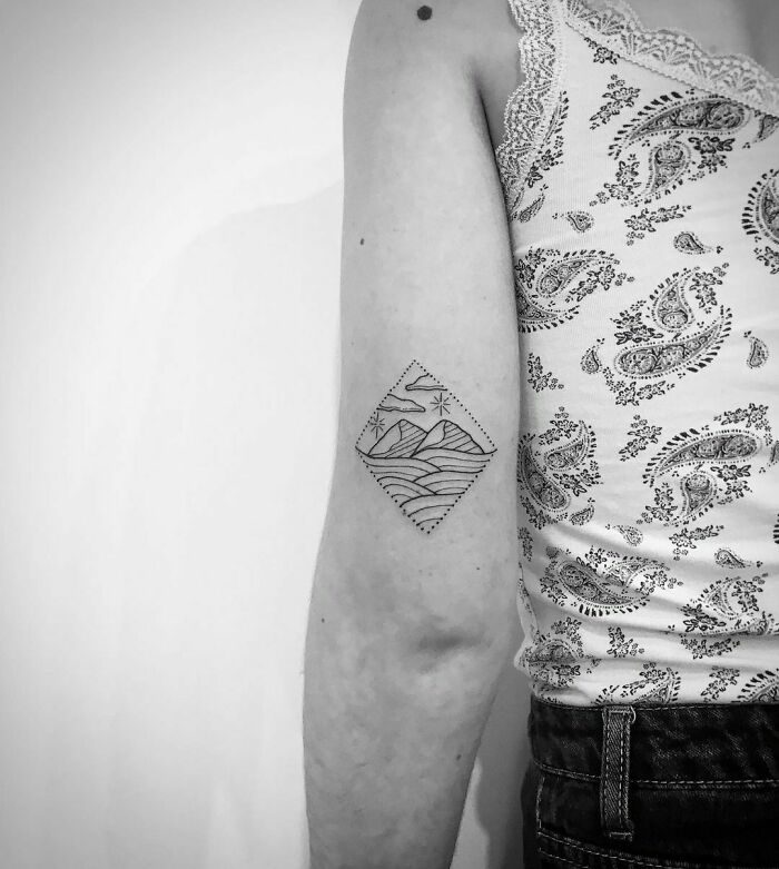 Arm featuring a geometric nature tattoo in black ink, showcasing mountains and waves.