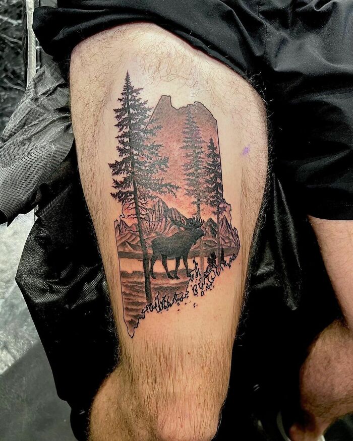 Nature tattoo featuring a moose and pine trees with a mountain backdrop on a person's thigh.