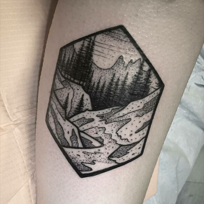Nature tattoo featuring a mountain landscape with trees and a river, celebrating the wonders of Earth.