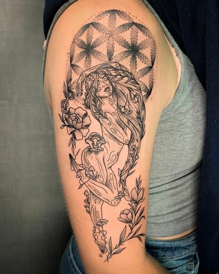 Arm with intricate nature tattoo featuring flowers and geometric patterns.