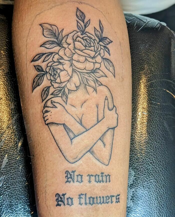 Tattoo of a headless figure with flowers and leaves, symbolizing nature, with text "No rain No flowers" on arm.