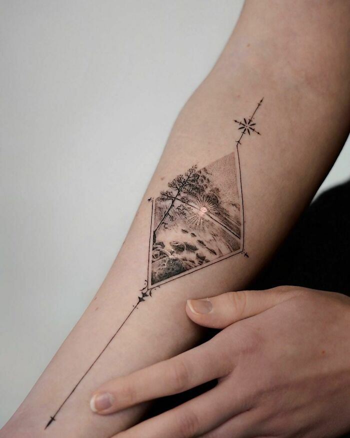 Nature tattoo depicting a scenic landscape on an arm, featuring trees and a sunburst design.