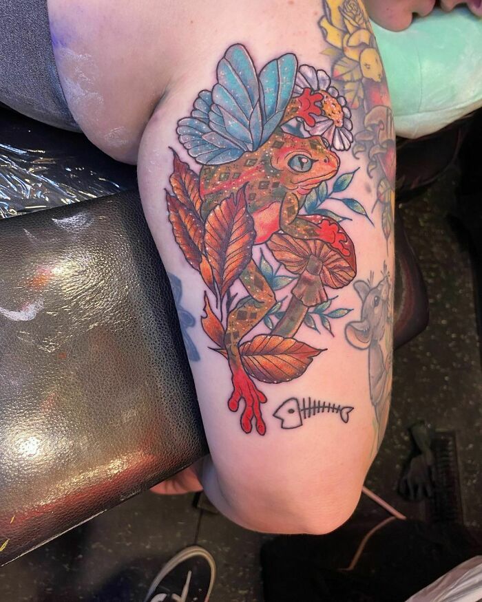Colorful nature tattoo featuring a frog with wings and vibrant mushrooms on an arm.