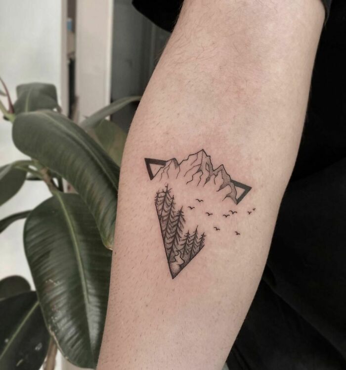 Nature tattoo of mountains and trees on arm, symbolizing the human-earth bond.