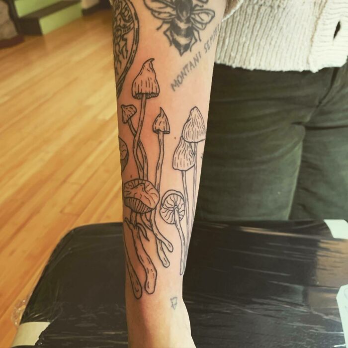 Arm with intricate nature tattoo of mushrooms and bee, symbolizing the human-earth bond through nature-inspired art.