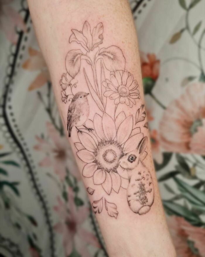 Nature tattoo of flowers, bird, and rabbit on an arm, celebrating the human-earth bond.