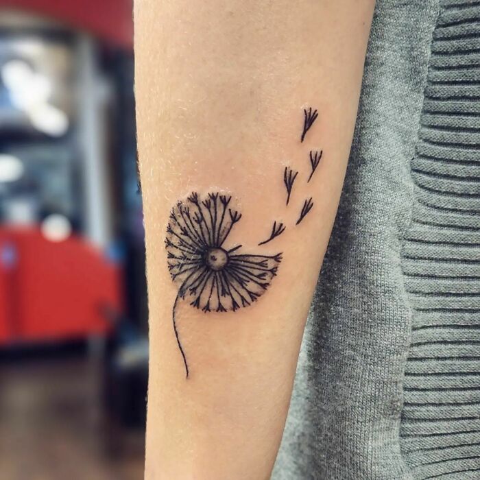 A dandelion tattoo on an arm, symbolizing the human-earth bond through nature-inspired art.