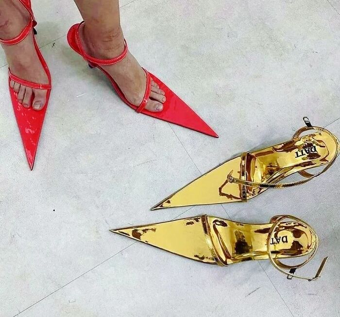 Red and gold weird shoes with extreme pointed tips on a light background.