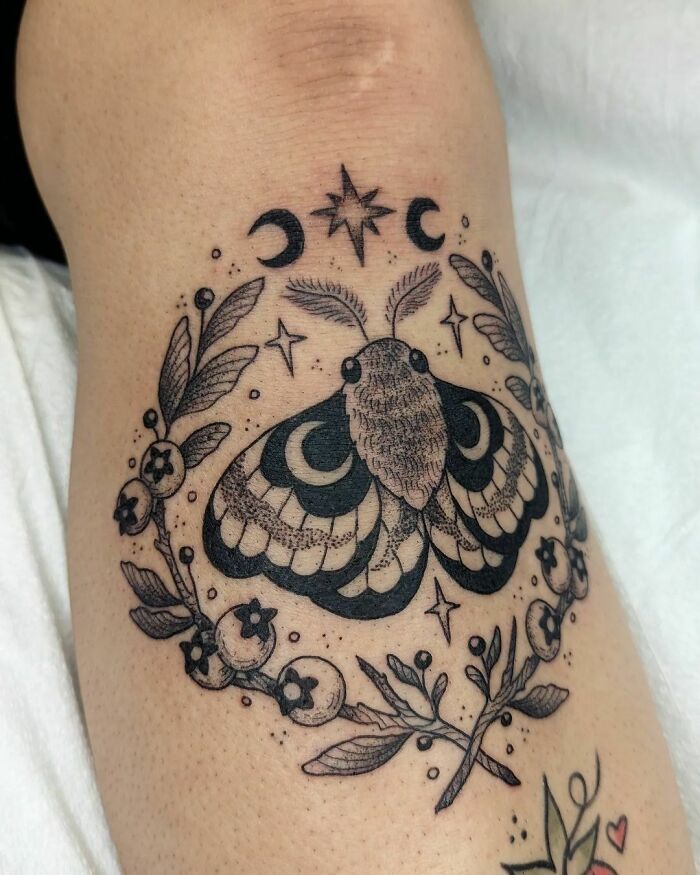 Tattoo of a moth with crescent moons, stars, and floral elements, symbolizing nature and a wild side.