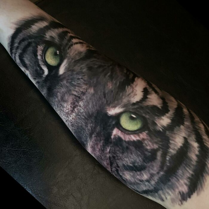 Close-up of a realistic tiger eye nature tattoo on a forearm.