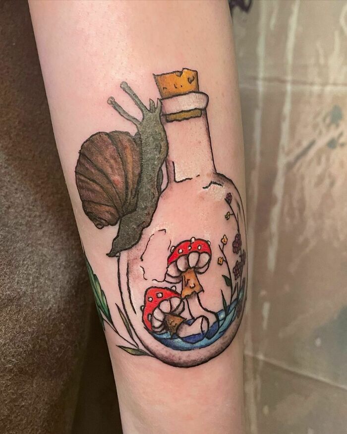 Nature tattoo featuring a snail on a bottle with mushrooms and flowers, symbolizing the human-earth bond.