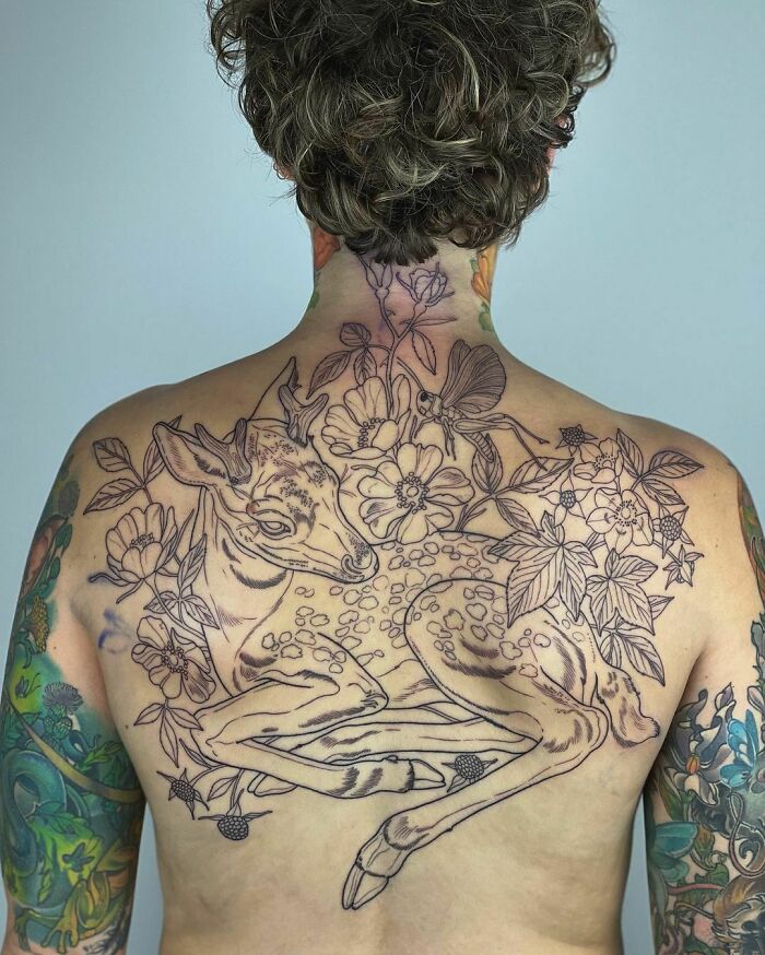 Back tattoo featuring a detailed fawn surrounded by flowers, showcasing nature tattoos with intricate linework.